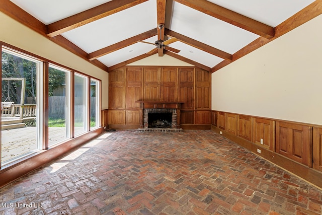 unfurnished living room featuring wooden walls, ceiling fan, a fireplace, and vaulted ceiling with beams