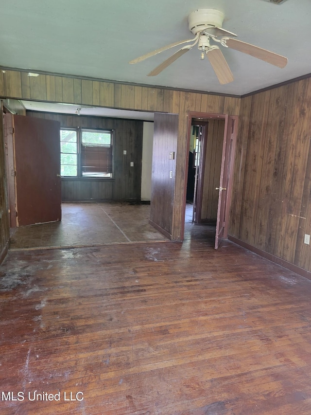 spare room featuring dark wood-type flooring, ceiling fan, and wood walls