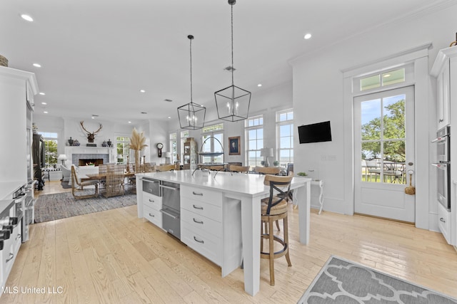 1221 E Beach Blvd, Pass Christian, MS 39571 - kitchen featuring open floor plan, a warm lit fireplace, a breakfast bar area, white cabinetry, and light wood-style floors