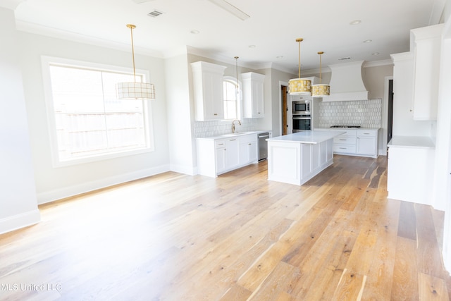 kitchen featuring white cabinets, a kitchen island, light wood-type flooring, custom range hood, and pendant lighting