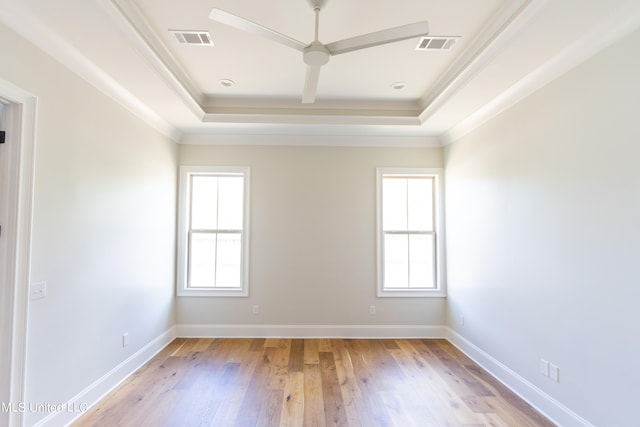 unfurnished room with a wealth of natural light, crown molding, a tray ceiling, and light wood-type flooring