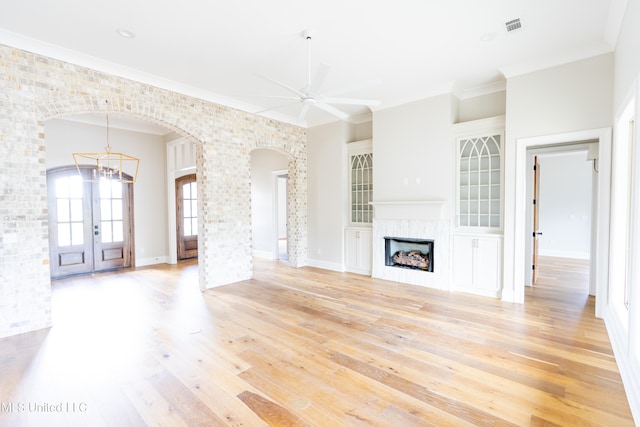 unfurnished living room featuring light hardwood / wood-style floors, french doors, ornamental molding, and ceiling fan with notable chandelier