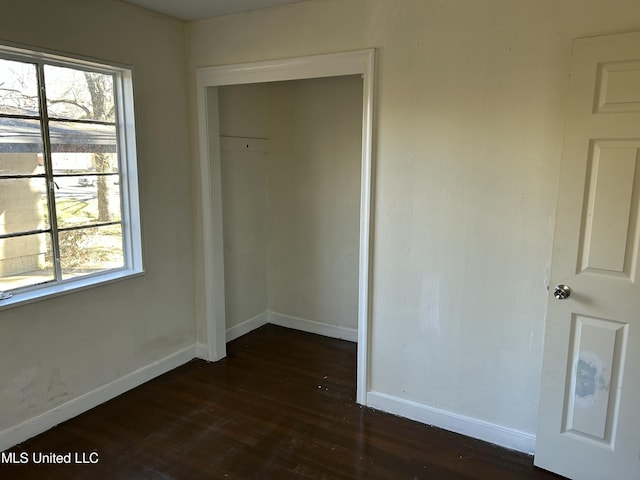 unfurnished bedroom with a closet, baseboards, and dark wood-style flooring