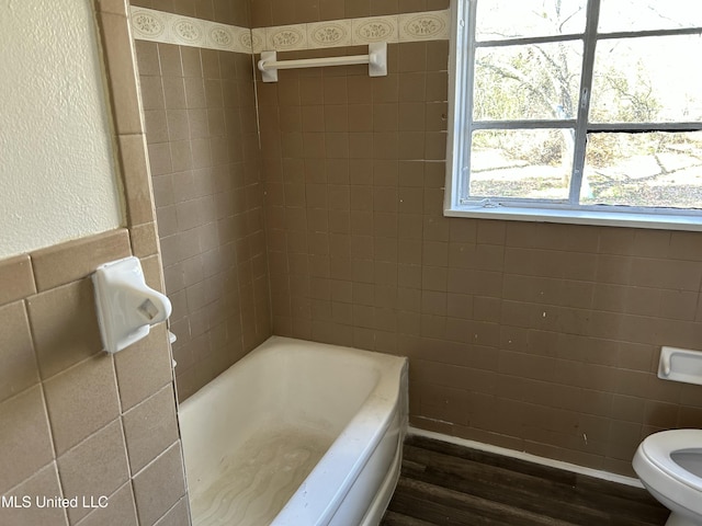 bathroom with wood finished floors, a tub, a shower, tile walls, and toilet