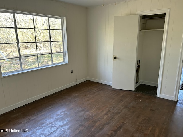 unfurnished bedroom featuring dark wood-style floors, a closet, and baseboards