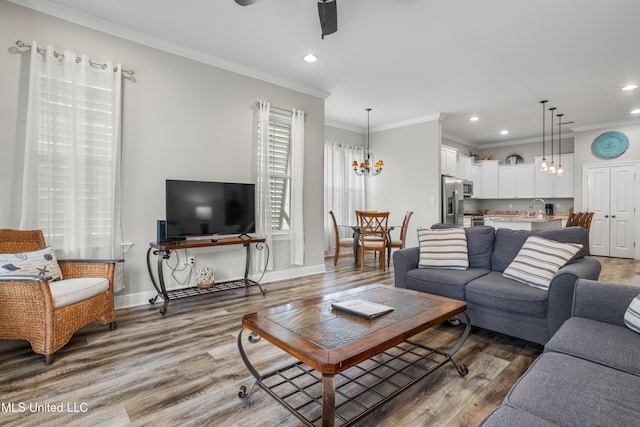 living room with hardwood / wood-style floors, ornamental molding, ceiling fan with notable chandelier, and sink