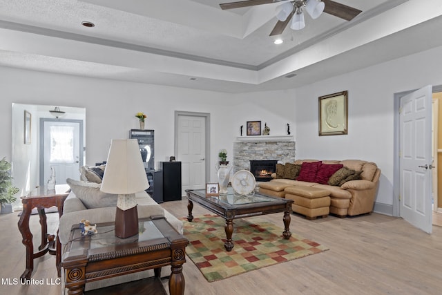 living room with a raised ceiling, ceiling fan, light wood-type flooring, a textured ceiling, and a fireplace