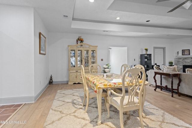 dining room with a fireplace, ceiling fan, light hardwood / wood-style flooring, and a textured ceiling