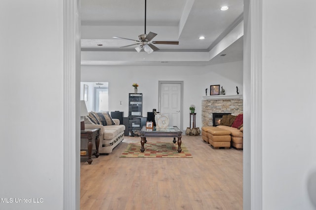 living room featuring a fireplace, wood-type flooring, a tray ceiling, and ceiling fan