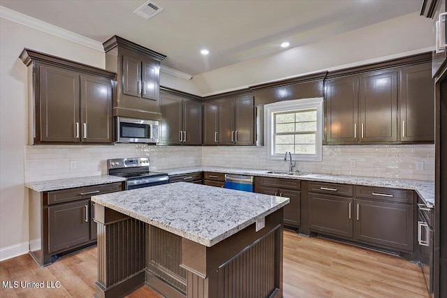 kitchen featuring sink, light wood-type flooring, a kitchen island, backsplash, and stainless steel appliances