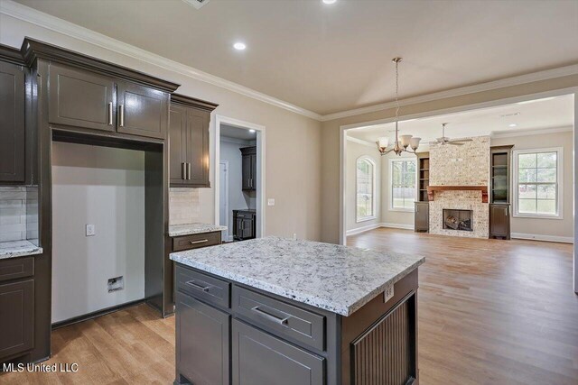 kitchen with backsplash, ornamental molding, a stone fireplace, a center island, and light hardwood / wood-style floors