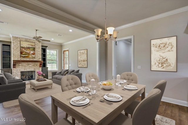 dining room featuring ceiling fan with notable chandelier, crown molding, hardwood / wood-style flooring, and a fireplace