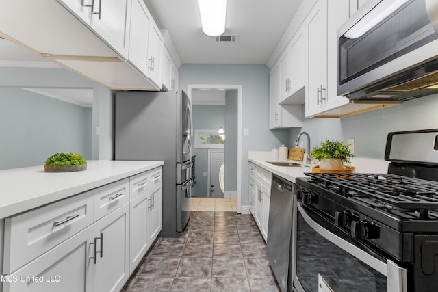 kitchen with tile patterned floors, white cabinets, sink, crown molding, and appliances with stainless steel finishes