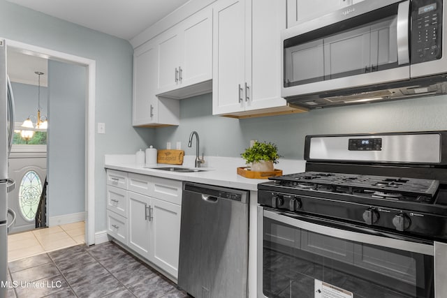 kitchen with stainless steel appliances, sink, dark tile patterned floors, a notable chandelier, and white cabinets