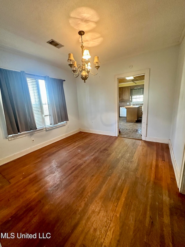 unfurnished dining area featuring a textured ceiling, a chandelier, and hardwood / wood-style floors