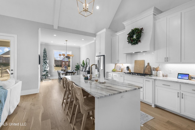 kitchen with a kitchen island with sink, hanging light fixtures, white cabinetry, a kitchen breakfast bar, and a chandelier