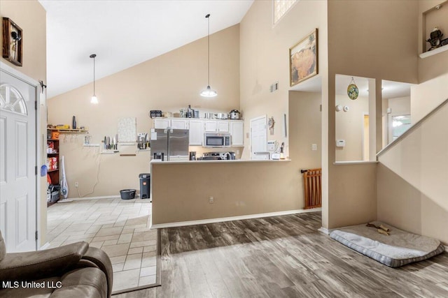 kitchen featuring high vaulted ceiling, hanging light fixtures, appliances with stainless steel finishes, and kitchen peninsula