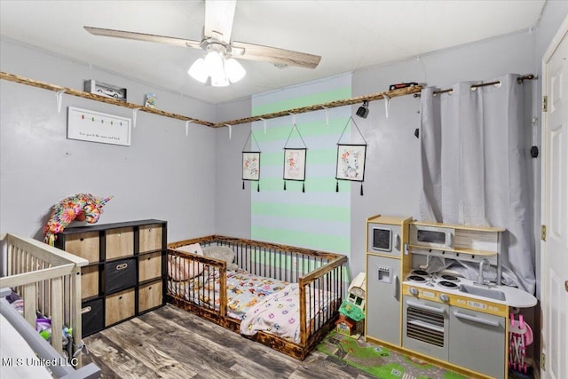 bedroom with hardwood / wood-style flooring, ceiling fan, and a nursery area