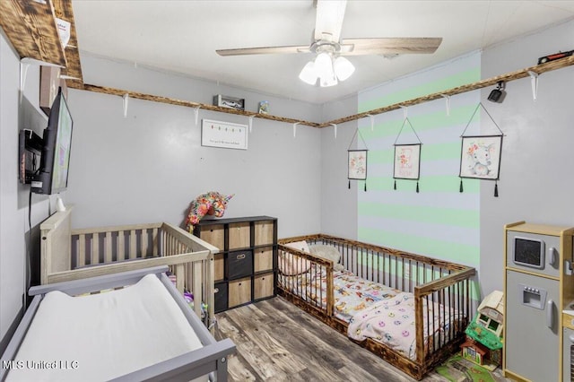 bedroom with ceiling fan, hardwood / wood-style floors, and a crib