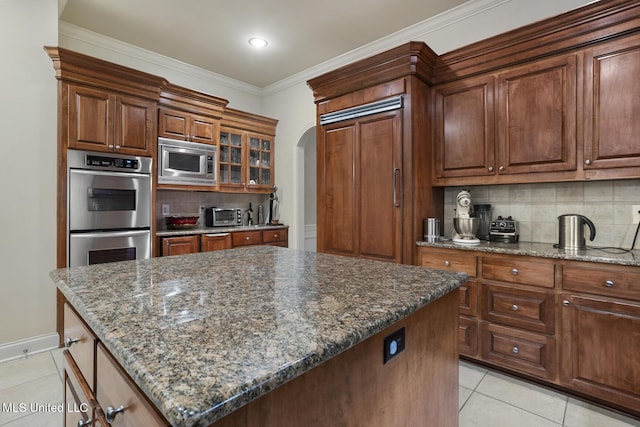 kitchen with stainless steel appliances, light tile patterned flooring, a center island, and dark stone countertops