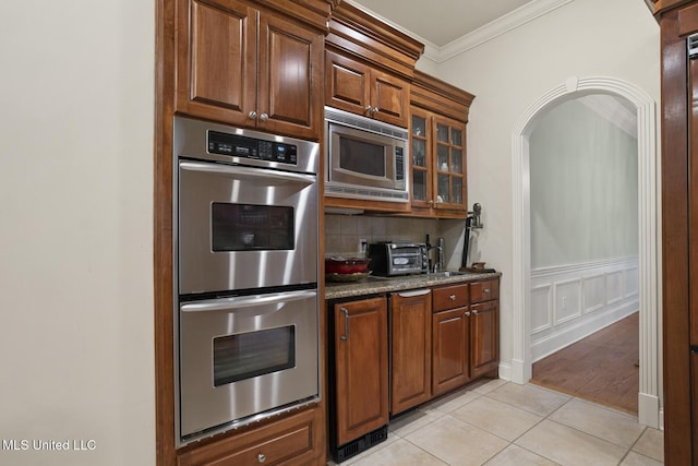 kitchen featuring crown molding, appliances with stainless steel finishes, stone countertops, decorative backsplash, and light tile patterned flooring