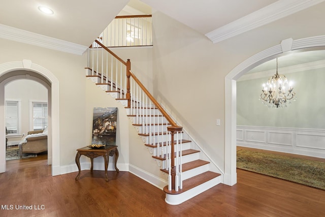 stairs featuring ornamental molding, wood-type flooring, and an inviting chandelier