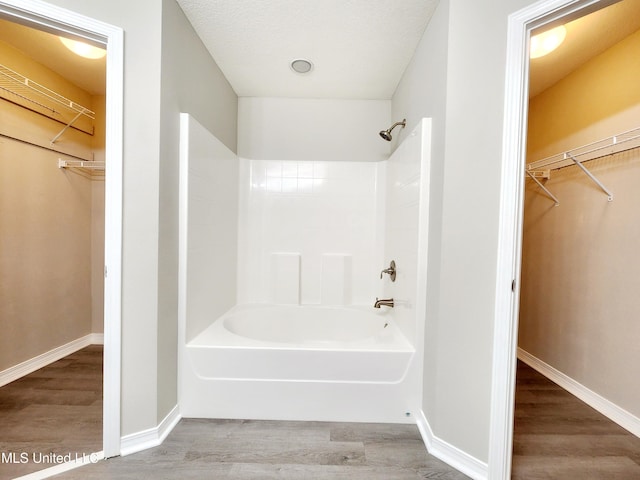 bathroom with baseboards, a walk in closet,  shower combination, and wood finished floors