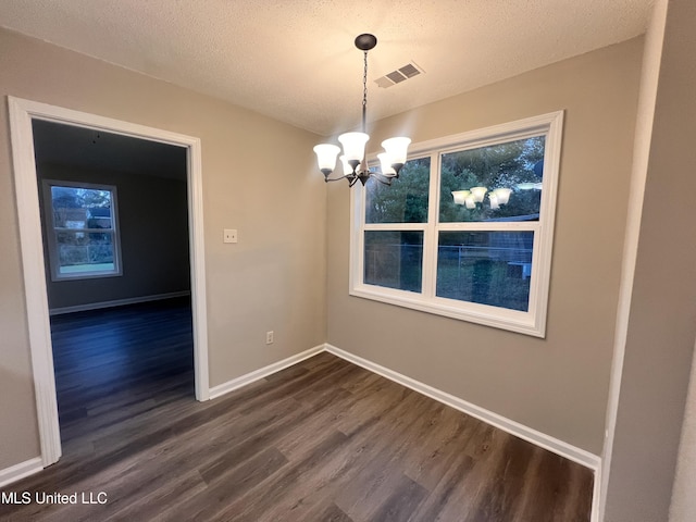 unfurnished dining area featuring a textured ceiling, dark hardwood / wood-style floors, and an inviting chandelier