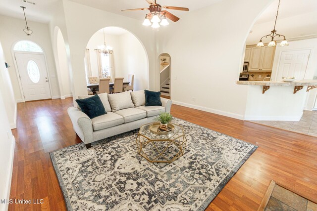 living area with light wood-style floors, arched walkways, ceiling fan with notable chandelier, and stairway