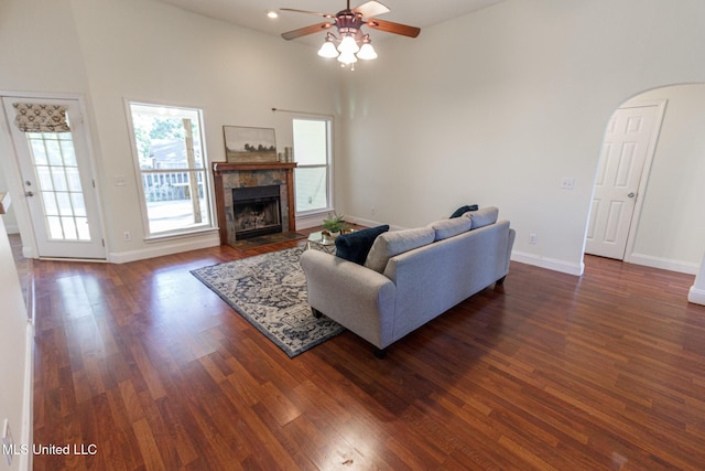living room featuring dark wood-style flooring, a ceiling fan, arched walkways, and a fireplace