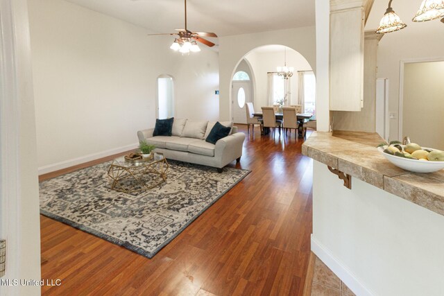living area with dark wood-style flooring, arched walkways, baseboards, and ceiling fan with notable chandelier
