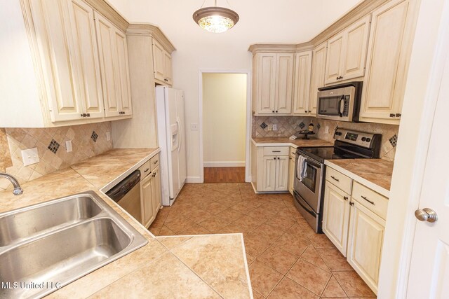 kitchen featuring decorative backsplash, appliances with stainless steel finishes, cream cabinets, a sink, and baseboards