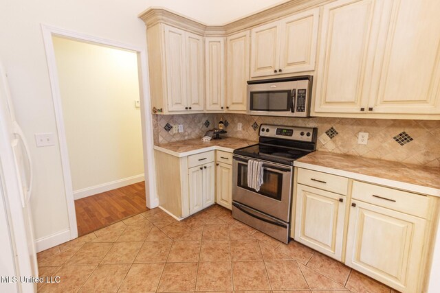 kitchen featuring light countertops, decorative backsplash, cream cabinetry, and stainless steel appliances