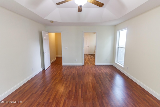 unfurnished bedroom featuring a ceiling fan, baseboards, dark wood finished floors, and a raised ceiling