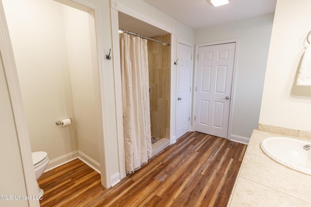 bathroom featuring a sink, wood finished floors, a tile shower, and toilet