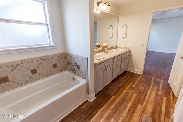 full bathroom featuring a sink, a bath, double vanity, and wood finished floors