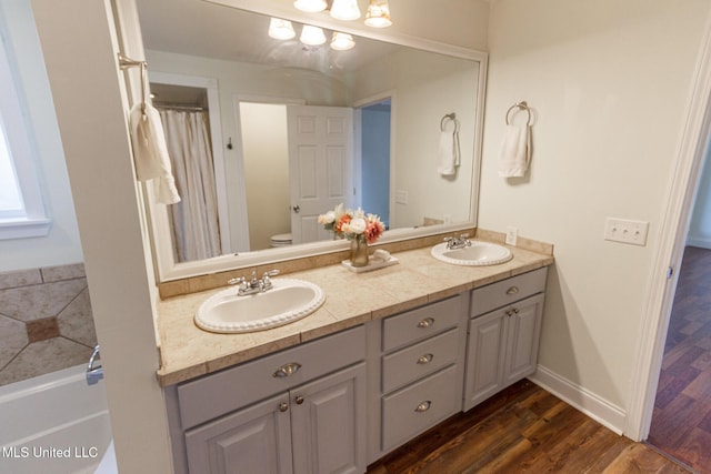 full bath featuring double vanity, toilet, a sink, and wood finished floors