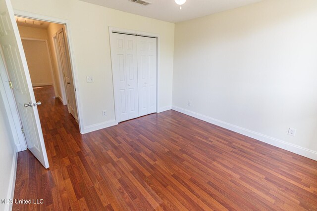 unfurnished bedroom featuring baseboards, visible vents, dark wood-style floors, and a closet