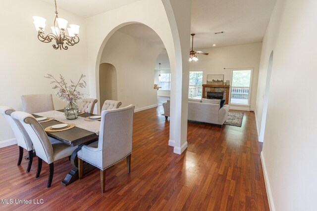 dining room with a fireplace, baseboards, ceiling fan with notable chandelier, and dark wood-type flooring