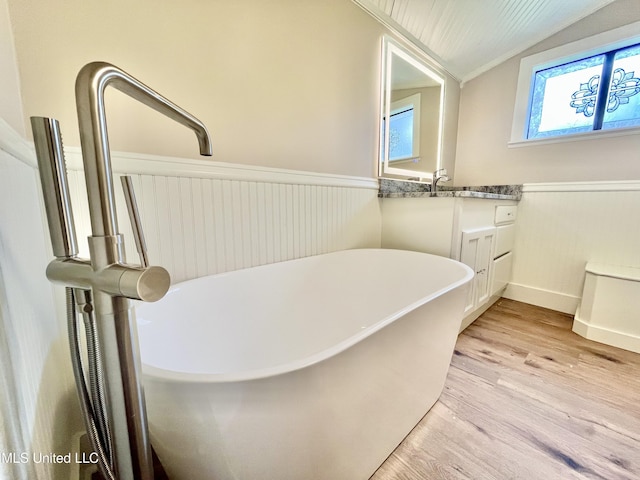 708 Lee Ave, Crystal Springs, MS 39059 - full bathroom with lofted ceiling, a wainscoted wall, a soaking tub, wood finished floors, and vanity