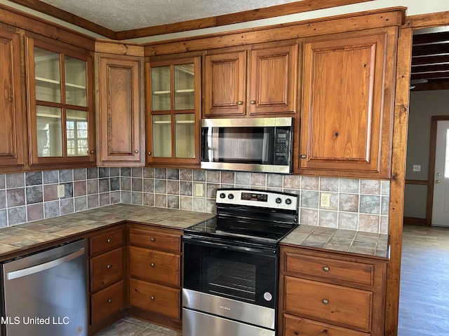 kitchen featuring tile countertops, backsplash, light hardwood / wood-style flooring, a textured ceiling, and appliances with stainless steel finishes