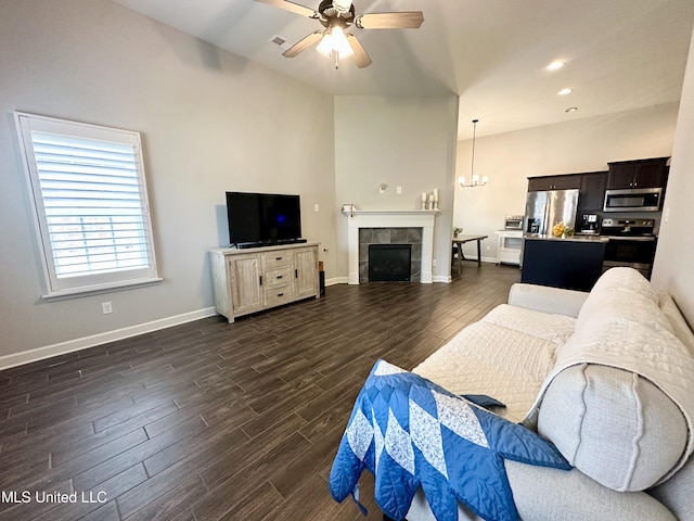 living room featuring dark wood-type flooring, a ceiling fan, baseboards, a fireplace, and a chandelier