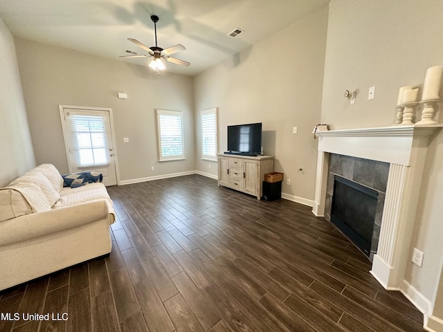 living area featuring dark wood-style floors, a ceiling fan, baseboards, and a tile fireplace