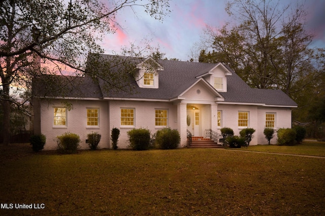 cape cod-style house featuring a shingled roof, a front yard, and brick siding