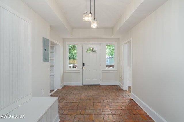 foyer entrance featuring a tray ceiling, brick floor, electric panel, and baseboards