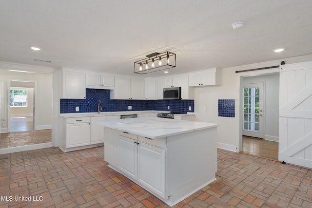 kitchen featuring brick floor, stainless steel microwave, decorative backsplash, a barn door, and white cabinetry