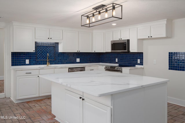 kitchen with brick floor, decorative backsplash, appliances with stainless steel finishes, white cabinetry, and a sink