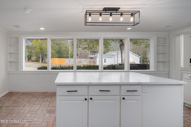 kitchen with brick floor, light countertops, ornamental molding, and white cabinetry