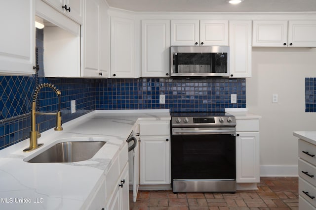 kitchen with appliances with stainless steel finishes, white cabinets, a sink, and backsplash