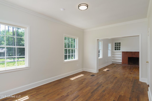 spare room with wood finished floors, visible vents, baseboards, a brick fireplace, and crown molding